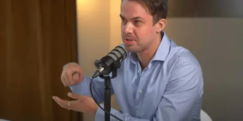 Michael van de Poppe w niebieskiej koszuli mówi do mikrofonu, gestykulując.