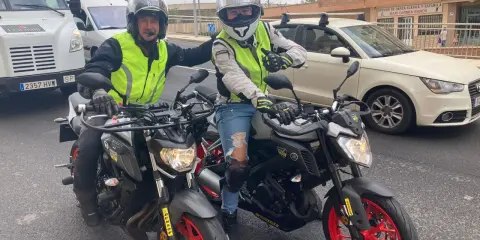 Dos motoristas con chalecos reflectantes y cascos posan con sus motos. Uno hace un gesto de "pulgar arriba". ¡Listos para la aventura en su a1 de moto!