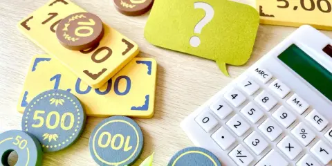 Jouets représentant des billets et des pièces, avec une calculatrice et un point d'interrogation. Une aide visuelle pour comprendre la fiscalité PEL.