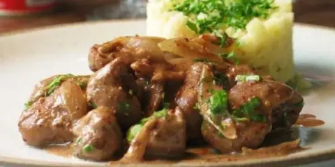 Une assiette de fricassée de rognons de veau, tendres et savoureux, accompagnés d'une purée de pommes de terre onctueuse et garnie de persil frais.