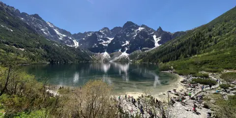 Widok na Morskie Oko z górami w tle i turystami na brzegu.