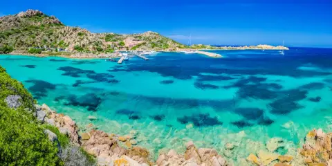 Acque cristalline e rocce granitiche ti aspettano per una visita alla Maddalena. Un paradiso azzurro con barche all'ancora.