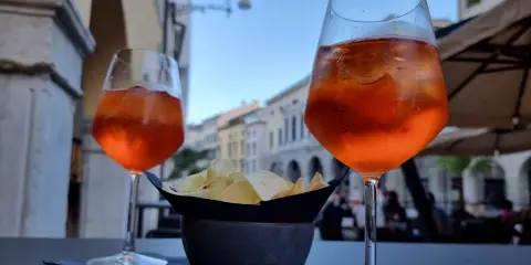 Dwa drinki Aperol Spritz i miseczka chipsów na stoliku. Czy alkohol podnosi cholesterol? To pytanie zadaje sobie wielu, delektując się takimi przekąskami.