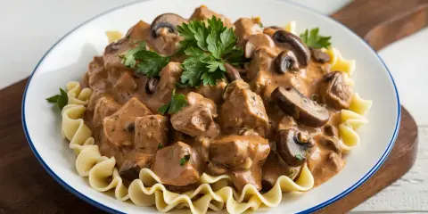 Un plat de boeuf Stroganoff crémeux avec des champignons et des pâtes ondulées, garni de persil frais. Un délice réconfortant.