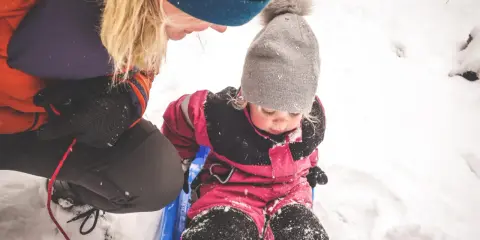 En vuxen drar ett barn på en pulka i snön. Ett perfekt exempel på friluftsliv barn.