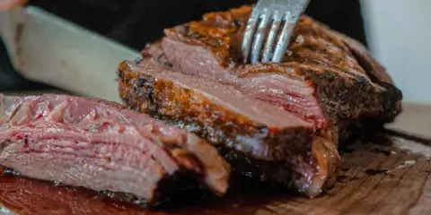 Un succulento arrosto di maiale, tagliato a fette su un tagliere di legno, con una forchetta che affonda nella carne tenera.