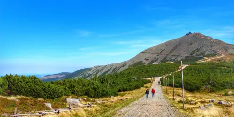 Kamienista ścieżka prowadzi na szczyt Śnieżki. Turyści idą w kierunku górskiej budowli.