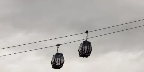 Kolejka na Gubałówkę w godzinach popołudniowych, dwie gondole wiszą na linach na tle pochmurnego nieba.