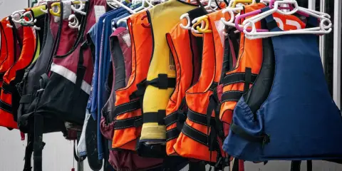 Chalecos salvavidas de varios colores, como naranja, amarillo y azul, colgados en perchas. Listos para la aventura, estos chalecos son de epis categoria 2.