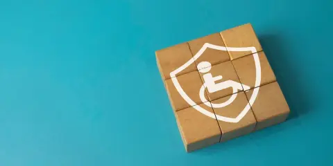 Drewniane klocki tworzą tarczę z symbolem osoby na wózku inwalidzkim. To symbol tego, co daje orzeczenie o niepełnosprawności – wsparcie i ochronę.