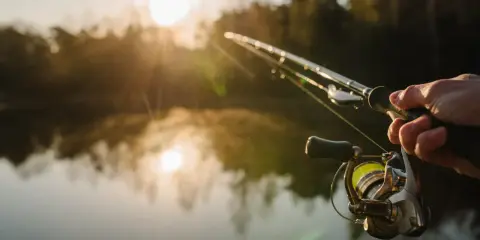 Poranek nad jeziorem, słońce wschodzi, mgła unosi się nad wodą. Dłoń trzyma wędkę, gotową do łowienia. To idealny moment na street fishing.