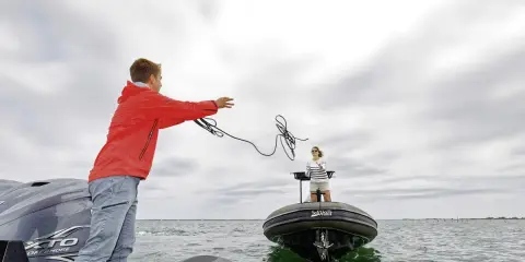 Un jeune homme lance une corde pour le remorquage d'un bateau en panne. Une femme attend sur l'autre embarcation.