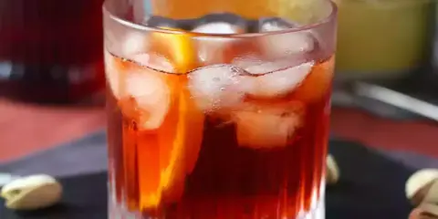 Orzeźwiający negroni sbagliato z lodem i plasterkiem pomarańczy, podany z pistacjami.
