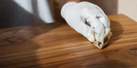Main d'une personne portant un gant blanc, cirant un meuble en bois après décapage. La cire donne un éclat subtil au bois.