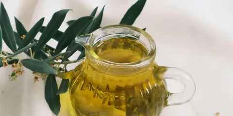 Aceite de oliva dorado en jarra de cristal, junto a rama de olivo. ¿Cuál es el aceite de oliva más suave?