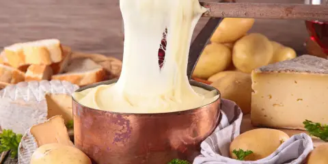 Fondue au fromage, un délice des spécialités culinaires auvergnates, avec du pain, des pommes de terre et du vin rouge.
