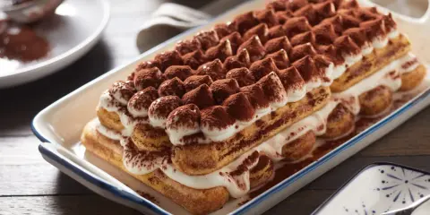 Un délicieux tiramisu, un dessert italien parfait pour un boudoir gourmand, est présenté dans un plat rectangulaire, saupoudré de cacao.