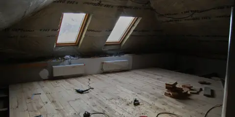 Chantier sous les combles : pose du frein vapeur, deux fenêtres de toit, radiateurs et outils sur le plancher en bois.