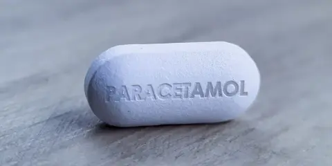 Biała tabletka z napisem "PARACETAMOL" na szarym tle. Dylemat: apap czy paracetamol?