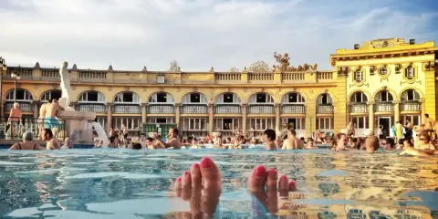 Fötter sticker upp ur vattnet i ett soligt budapest spa. Människor badar och njuter av den vackra arkitekturen.