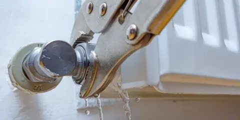 Pinzas sujetan una conexión de un radiador que gotea, con agua cayendo.
