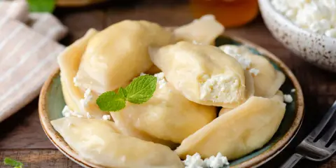 Pyszne pierogi z serem, udekorowane miętą i posypane białym serem. Obok słoiczek miodu i miseczka z serem.