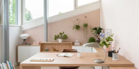 Une petite chambre avec bureau, lumineuse et décorée de plantes. Le bureau en bois clair est prêt pour le travail ou la lecture.