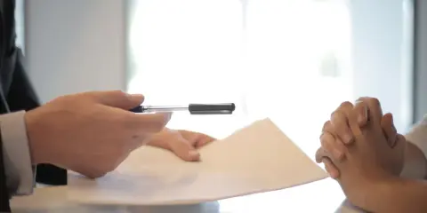 Dłonie trzymają dokumenty i długopis. Przygotowanie do napisania listu motywacyjnego dla referenta biurowego.