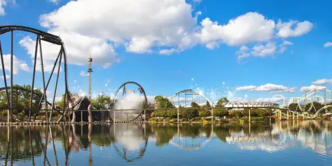 Aussicht auf Achterbahnen und einen Freizeitpark mit Spiegelung im Wasser.
