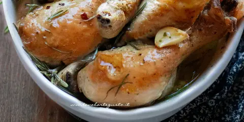 Succulente cosce di pollo al forno, dorate e profumate al rosmarino e aglio, servite in una ciotola bianca.