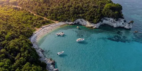 Baia con acque cristalline e vegetazione lussureggiante, ideale per famiglie. Diverse barche ormeggiate, perfette per esplorare le isole greche.