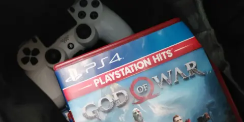 Dos mandos de PS4 y la carátula del juego "God of War", uno de los juegos exclusivos de PS4 más aclamados.