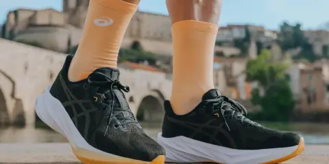 Biegacz w pomarańczowych skarpetkach z logo Asics i ciemnych butach tej firmy, gotowy do podboju miasta.