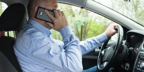 Mężczyzna za kierownicą rozmawia przez telefon, co może skończyć się mandatem.