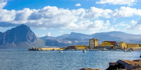 La tonnara di Bonagia, con il suo porto e le montagne sullo sfondo, sotto un cielo azzurro e nuvoloso.