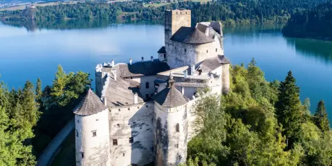 Zamek Dunajec, majestatyczna twierdza na skale, otoczona zielenią i błękitną wodą jeziora.