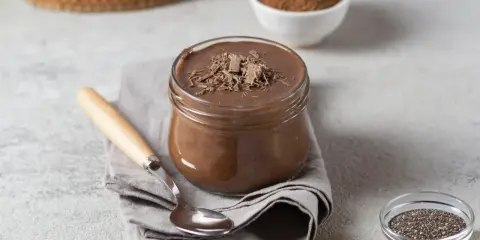 Pudding proteinowy z czekoladą, idealny na deser. Obok nasiona chia i kakao, sugerujące, z czym jeść.