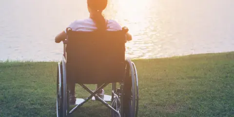 Osoba na wózku inwalidzkim, z orzeczeniem o niepełnosprawności, cieszy się zachodem słońca nad jeziorem. Zasiłek pielęgnacyjny zapewnia wsparcie.