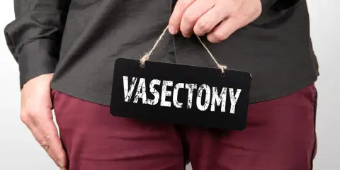 Mężczyzna trzyma tabliczkę z napisem "VASECTOMY". Czy po wazektomii można mieć dzieci? To pytanie nurtuje wielu.