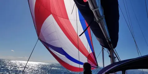 Voile colorée gonflée par le vent, un tableau longueur sandows sur fond de mer scintillante et ciel bleu.