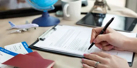 Ręka podpisuje dokumenty, obok paszporty, bilety lotnicze i globus. Planujesz podróż do Chorwacji i potrzebujesz zielonej karty?