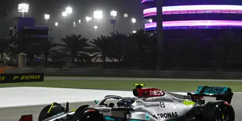 Silberner F1-Rennwagen mit Petronas-Sponsoren fährt bei Nacht auf der Rennstrecke in Bahrain. Flutlicht und ein beleuchtetes Gebäude im Hintergrund.