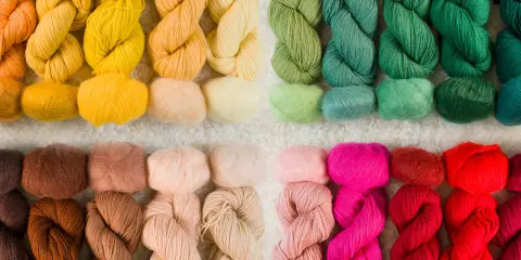 Ett urval av garn i olika färger, från varma orange och gula toner till gröna, rosa och röda nyanser. Perfekt för ditt nästa projekt med garn lin.