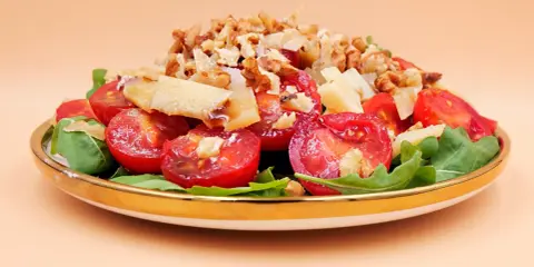Pyszna sałatka z rukolą, pomidorkami koktajlowymi, parmezanem i orzechami włoskimi, podana na złotej zastawie.