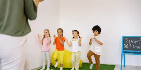 Dzieci ćwiczą przy tablicy z napisem "Sport time". Krótkie hasła sportowe dla dzieci motywują do ruchu.