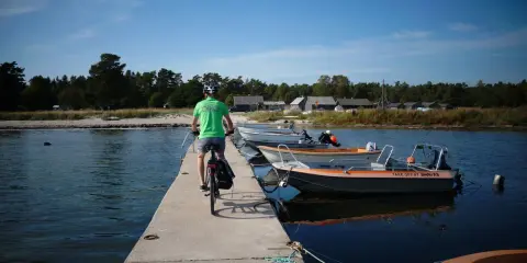 En cyklist på en brygga med båtar vid en svensk kust. Perfekt för att utforska cykelleder Sverige.