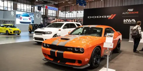 Pomarańczowy Dodge Challenger Hellcat z szarymi pasami na masce, obok białego SUV-a Dodge Durango.