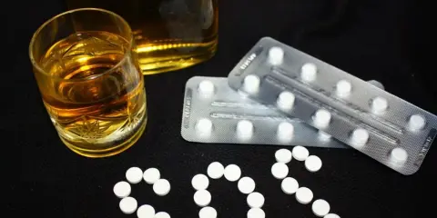 Szklanka alkoholu i blistry z tabletkami układają się w napis SOS. Czy to pytanie o benzodiazepiny, co to jest i jakie ryzyko niesie ich połączenie z alkoholem?