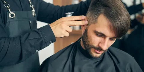Fryzjer dopracowuje męskie fryzury z grzywką do przodu, tworząc stylowy look.
