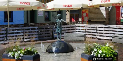 Fontanna z dziewczynką na kuli, otoczona donicami z kwiatami i parasolami. Urokliwe lubliniec atrakcje, idealne na spacer.
